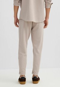 Pantalones beige con textura y corte relajado, con puños doblados y una cintura lisa. Combinados con zapatillas marrón oscuro.