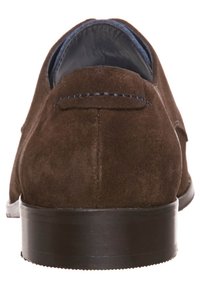 Chaussure en daim marron avec une texture lisse, une doublure en cuir et une semelle en caoutchouc foncé. Présente des coutures discrètes à l'arrière.