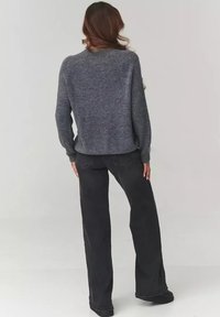 Szary, dziergany sweter z długim rękawem, luźny krój, okrągły dekolt, w połączeniu z czarnymi spodniami wysokim stanem i czarnym obuwiem, widok z tyłu.