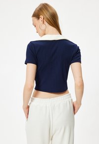 Top corto a coste di colore navy con colletto bianco a contrasto, maniche corte e design aderente. Abbinato a pantaloni larghi di colore chiaro.