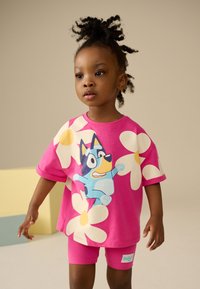 T-shirt in cotone rosa con grande stampa floreale e personaggio dei cartoni animati. Abbinata a pantaloncini rosa coordinati, con una piccola etichetta sul lato.