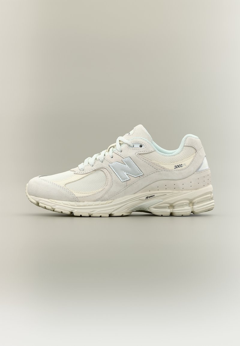 Basket blanche New Balance 2002R avec tige en mesh et suède, logo réfléchissant "N", semelle coussinée et semelle extérieure texturée sur fond neutre.