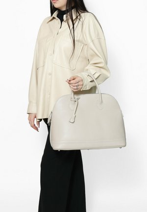 Lichtbeige handtas met een afgeronde silhouette, textuurleer, twee korte handvatten en een kwastje aan de rits.