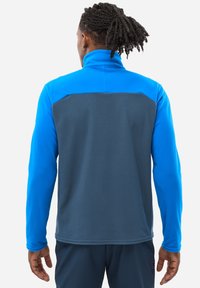Fleece-Jacke mit hohem Kragen, mit einem geteilten Design in leuchtendem Blau und dunklem Grau, langen Ärmeln und glatter Textur.