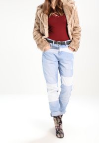 Beige bunda z umělé kožešiny, vínový top, světle modré kalhoty s bílými panely a květinové kotníkové boty. Viditelné texturované tkaniny a kontrastní detaily.