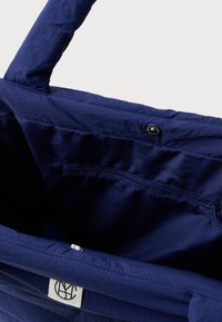 Námorníčky modrá látková taška s našitými okraji, vnitřní kapsou na zip, uzávěrem na patentní knoflík a malou bílou logovou visačkou uvnitř.