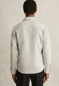 Cămașă lungă cu mânecă lungă de culoare gri deschis, cu o croială dreaptă, inclusiv o textură moale, manșete cu nasturi și guler fix.