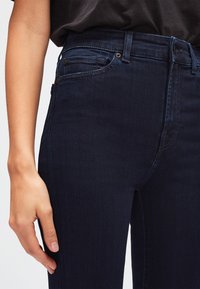 Jeans en denim bleu foncé au design ajusté, dotés d'une taille haute, de poches à l'avant et de détails de couture subtils le long des coutures.
