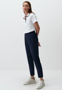 Witte polo met marineblauwe accenten, gecombineerd met marineblauwe tapered broek en witte sneakers. De outfit heeft een minimalistisch ontwerp en heeft een gladde textuur.