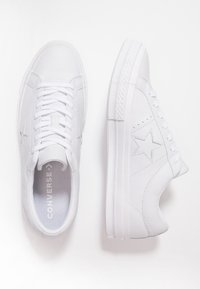 Baskets en cuir blanc avec lacets plats, semelles en caoutchouc et accents en forme d'étoile sur le côté. Texture lisse et design minimaliste.