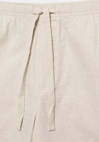 Beige linnenbroek met elastische tailleband en lange stoffen trekkoorden die aan de voorkant in een eenvoudige knoop zijn gebonden.