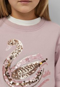 Roosa sweatshirt, millel on kuldse roosa, heleda roosa ja hõbeda toonides sädelustega luige kujundus, ribakrae ja -mansettidega.