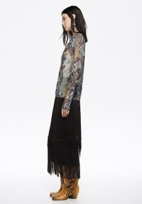 Bluzka z długim rękawem w niebiesko-brązowy wzór mozaiki, zestawiona z czarną spódnicą z frędzlami i botkami w wężowy wzór. Dodatki to pierścionki.