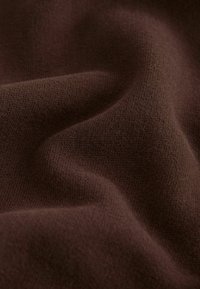 Tela tejida marrón suave con textura visible y pliegues suaves que crean una superficie lisa y ondulada.