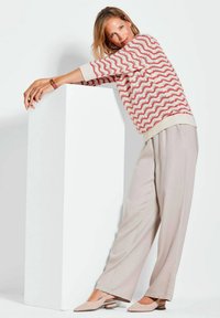 Strickpullover mit rotem Wellenmuster auf cremefarbener Basis; lockere beige Hose; weiche Textur; beigefarbene Slingback-Schuhe mit kleinem Absatz.