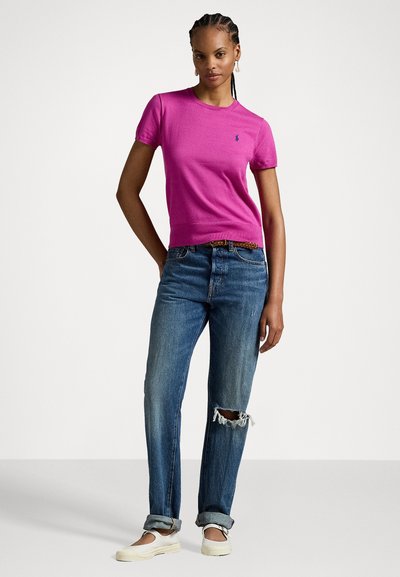 T-shirt fuchsia à manches courtes avec un col rond et un petit logo, associé à un jean bleu déchiré et à des chaussures à enfiler couleur crème clair.
