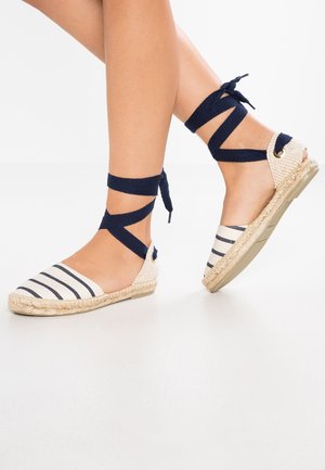 Gestreepte espadrille in beige en marineblauw, met bovenkant van canvas, gevlochten jute zool en wikkelbare stofriemen rond de enkel.