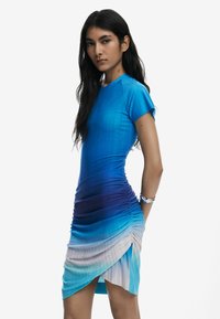 Form-fitting dress transitioning from bright blue to deep purple, featuring horizontal ruching and a diagonal hem detail. Smooth, stretchy fabric.