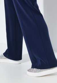 Marinblå vida byxor kombinerade med glittrande silverf�ärgade sneakers med strukturerad ovandel och vit gummiyttersula.