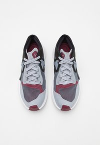 Sportowe sneakersy z szarą siatkową cholewką, czarnymi akcentami, bordowymi detalami i białą podeszwą, z teksturowanym wzorem na materiale.