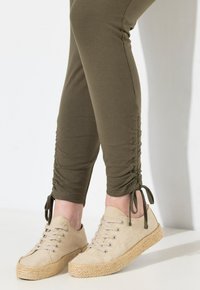Beige canvas espadriller med vävd jutesula och snördesign, tillsammans med olivgröna figurnära leggings som är samlade vid anklarna.