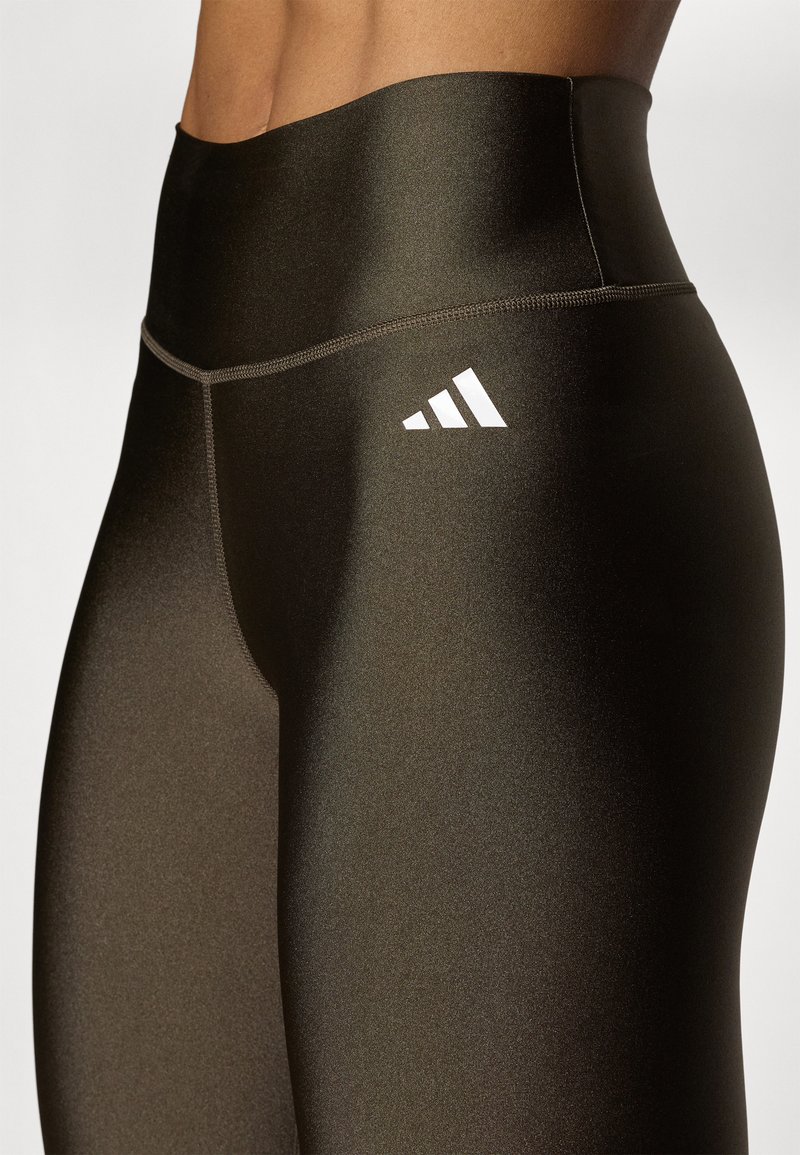 Hochtaillierte schwarze Leggings aus glänzendem, dehnbarem Stoff; mit einem weißen Adidas-Logo am Oberschenkel und Flachnähten für zusätzlichen Komfort.