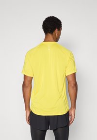 Camiseta atlética amarilla, hecha de un tejido ligero, con mangas cortas, cuello redondo y detalles reflectantes en la parte posterior.