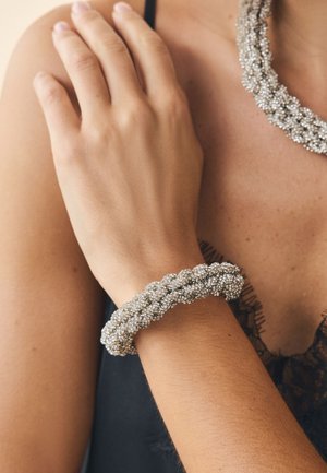 Metallic silver braided bracelet with a textured surface, featuring clusters of small beads, worn on the wrist.