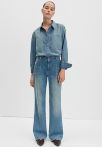 Chemise en denim bleu clair avec deux poches poitrine, associée à un jean large taille haute bleu clair. Texture lisse, coupe décontractée.