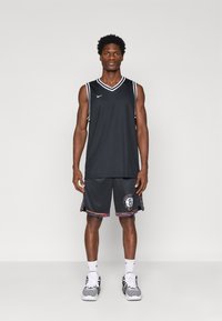 Camisa de basquetebol preta com detalhes brancos, combinada com calções pretos que apresentam um logótipo de Brooklyn e acabamentos multicoloridos nas laterais.
