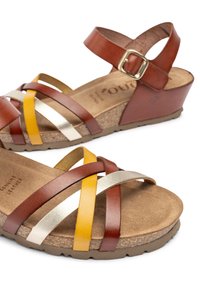 Sandali in pelle marrone e beige con cinturini incrociati in oro, argento e giallo. Suola in sughero con wedge e chiusura a fibbia. Suola piatta con texture.