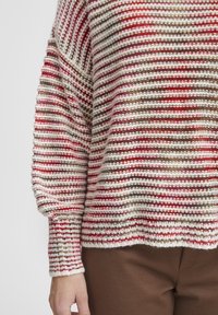 Randig tröja i röd, vit och brun garn. Stickad textur med lös passform och ribbade manschetter. Tröjan har en vid halsringning och sänkta axelsömmar.