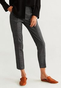 Pantalons ajustés à carreaux gris avec une coupe slim, ornés de bandes noires sur les côtés. Portés avec des chaussures brunes à enfiler et un haut noir ample.