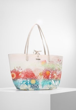 Cremefarbene Tragetasche mit doppelten Griffen, verziert mit pinken, orangefarbenen, blauen und weißen Blumenmustern, steht auf einem weißen Podest.