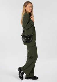 Borsa nera in pelle dalla forma curva, con dettagli in oro e perle, indossata con un completo verde e scarpe nere in vernice.