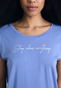 Ljusblå bomulls t-shirt med rund halsringning. Har vit kursiv text "Sömn löser allt" över bröstet.