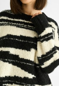 Black and white striped sweater made of textured knit fabric, featuring wide horizontal stripes and a relaxed fit with cuffed sleeves.