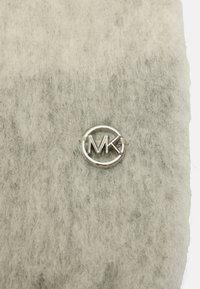 Szara filcowa tkanina z centralnym, okrągłym logo w kolorze srebrnym z inicjałami „MK”. Tekstura wydaje się miękka i puszysta.