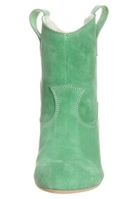 Bottes chevilles en daim vert à texture lisse, bout pointu et coutures renforcées. Équipées de languettes pour faciliter l'enfilage et de surpiqûres décoratives.