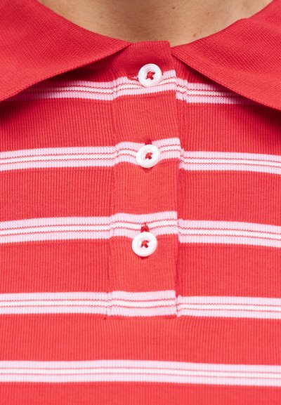 Κόκκινο και λευκό ριγέ πόλο με τρία λευκά κουμπιά κουμπωμένα μπροστά κάτω από το γιακά.
