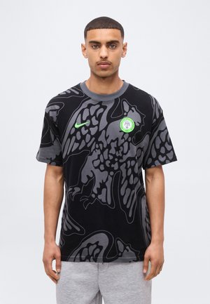 Jeune homme portant un t-shirt graphique Nike noir et gris avec un logo vert de la Fédération Nigériane de Football sur la poitrine.
