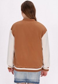 Giacca in corduroy marrone con maniche in pelliccia bianca, polsini e orlo a coste, e colletto classico. La vista posteriore mostra il contrasto di colore e la texture.