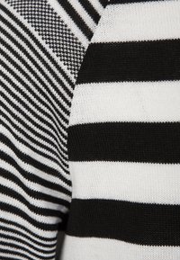 Tela de punto en blanco y negro a rayas que presenta diferentes anchos y texturas de las rayas, incluyendo líneas finas y secciones gruesas.