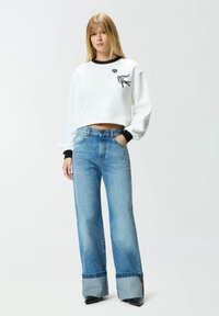 Felpa bianca corta con polsini neri che presentano un motivo ricamato nero. Jeans a gamba larga color azzurro chiaro con un dettaglio unico sul risvolto.