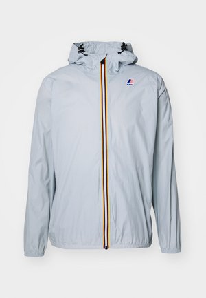 Világoskék széldzseki kapucnival, több színű függőleges cipzárral és egy kis logóval a mellkason. Sima textúra.