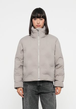 Lys grå puffjakke med høy krage, frontlukking med glidelås og quiltet tekstur. Kombinert med mørkegrå jeans.