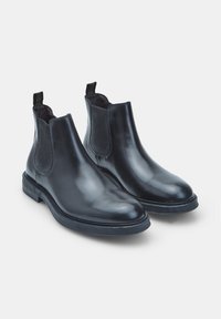 Botas Chelsea de cuero negro con paneles laterales elásticos, un acabado suave y una suela de goma plana con textura sutil.
