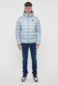 Giacca in piuma azzurro chiaro con zip anteriore, cappuccio e due tasche laterali. Presenta un design trapuntato e un piccolo logo del marchio sul petto.