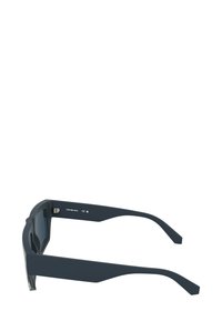 Occhiali da sole grigio scuro con un design elegante e angolare. Presentano lenti larghe, aste sottili e una finitura opaca. Marchio ben visibile sulla montatura.