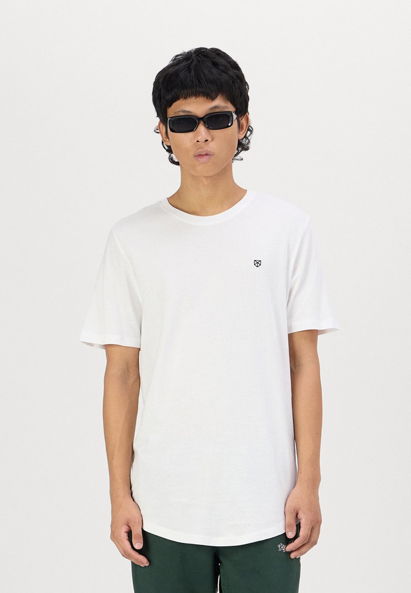 Weißes Baumwoll-T-Shirt mit Rundhalsausschnitt und kurzen Ärmeln, versehen mit einem kleinen schwarzen Logo auf der Brust, kombiniert mit schwarzen Sonnenbrillen.